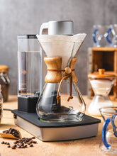 Coffee brewing setup with a glass carafe and wooden collar on a wooden surface.