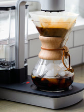 Iced coffee being brewed using a glass carafe with wooden collar on a kitchen counter.