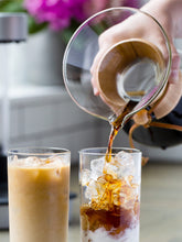 Person pouring iced coffee into two glasses with a blurred background