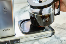 Moccamaster coffee maker on a marble countertop with a person holding the carafe.