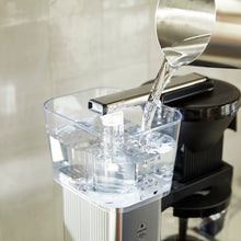 Clear pitcher being filled with water from a faucet on a kitchen counter.