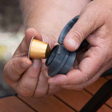 Close-up of hands holding a gold and gray coffee capsule.