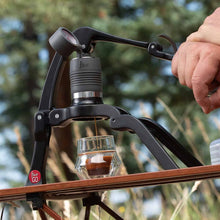 Person using a portable coffee press outdoors with trees in the background