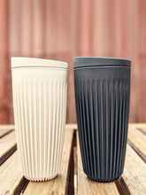 Two ribbed ceramic tumblers, one white and one black, on a wooden surface with a blurred background.