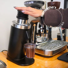 Person using a coffee grinder with a coffee machine in the background